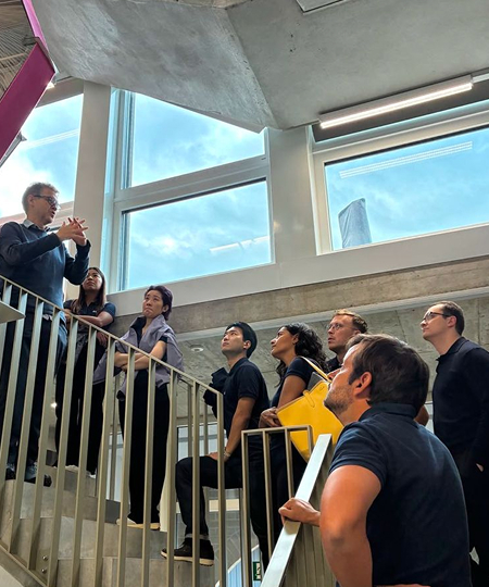 A group of people standing on stairs inside a building, engaged in conversation and looking around.