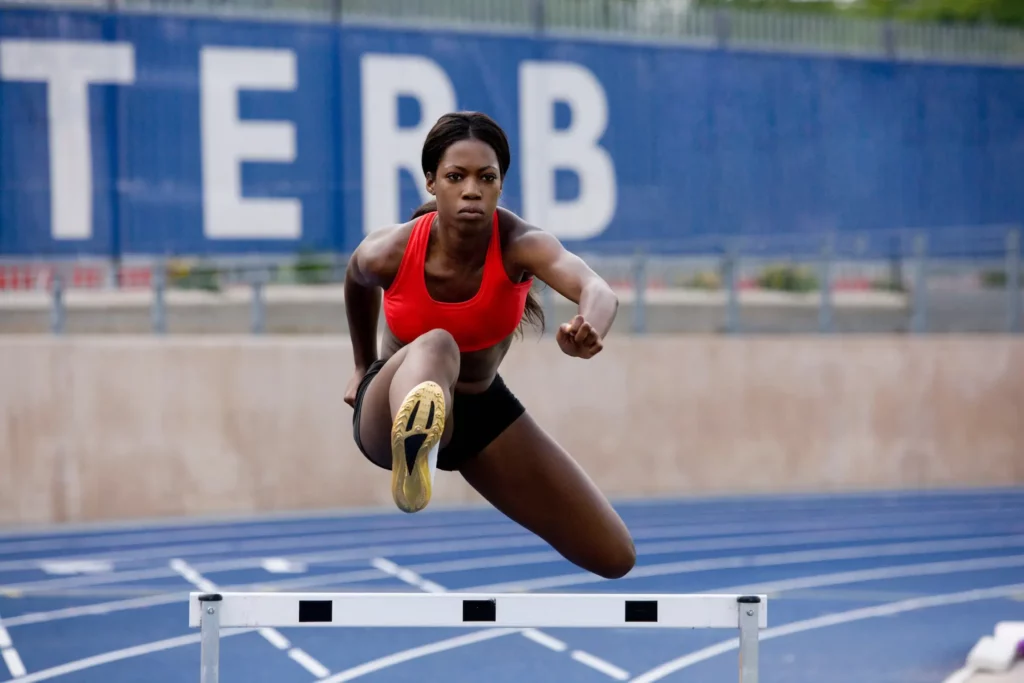 female runner jumping over a hurdle on olympic tracks