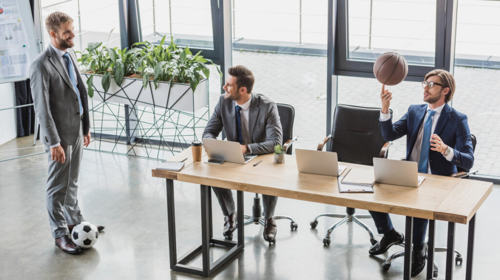 Business professionals in a modern office discussing strategy with sports equipment present, symbolizing career transitions from traditional industries into sport management roles.