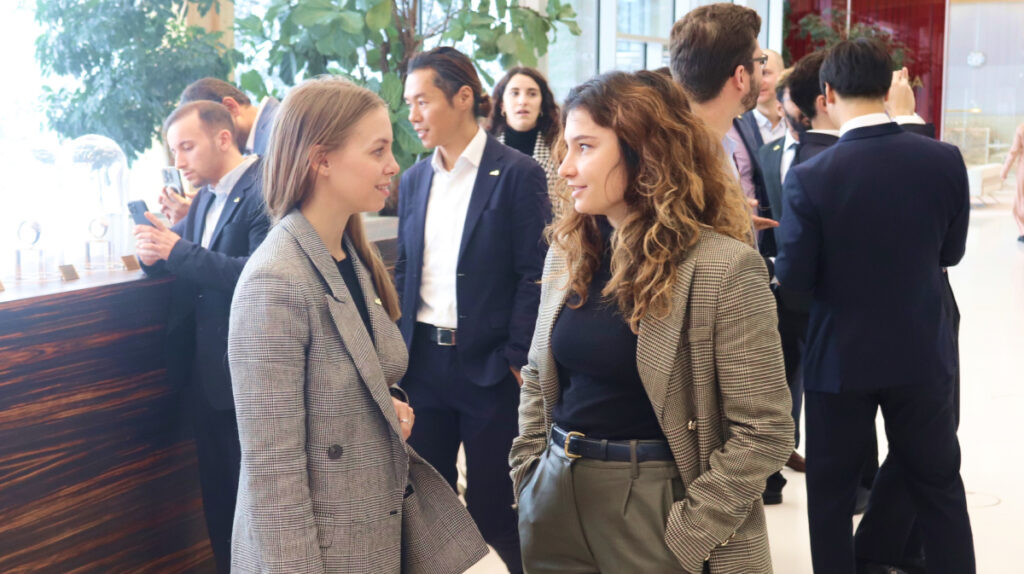 Two professional women in business attire talking at a networking event, representing professional collaboration and relationship building within the sport management industry.