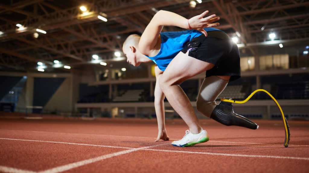 Para athlete with running blade on indoor track field in starting position, ready to run demonstrating inclusive sport technology