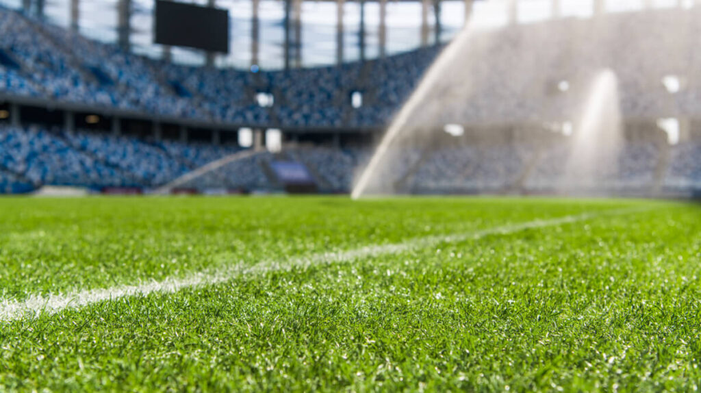 Close-up of stadium pitch with automated sprinklers irrigating grass, illustrating sustainable water management and sport innovation in maintaining high-quality playing surfaces
